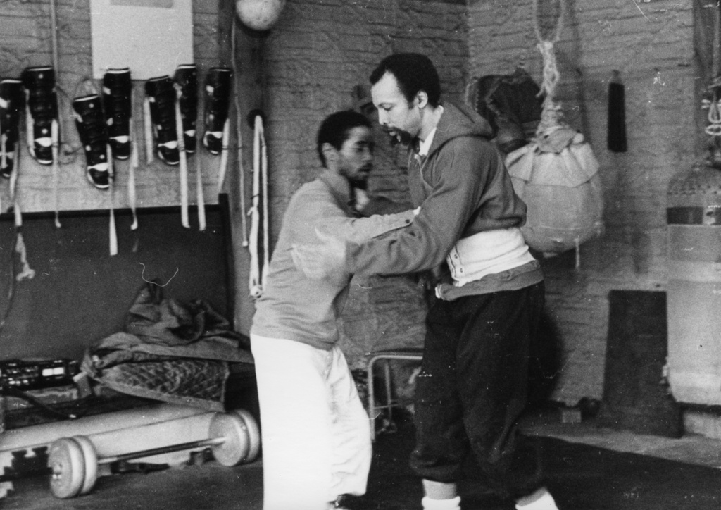 A black and white photograph of two men in a dojo. They are photographed while performing Yara, a martial arts technique created by Milford Graves.