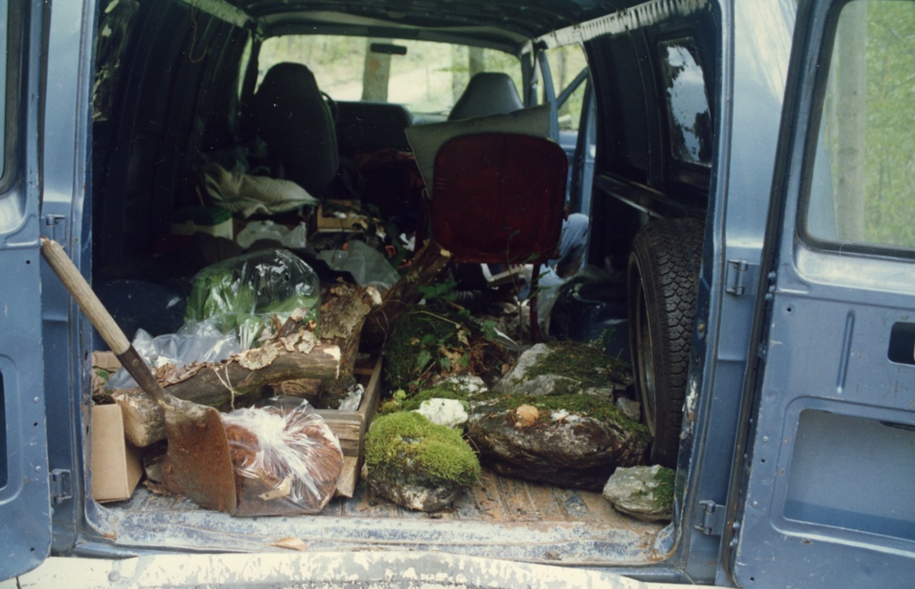 The inside of a blue van filled with mossy rocks, soil, and a dirt covered shovel.&nbsp;